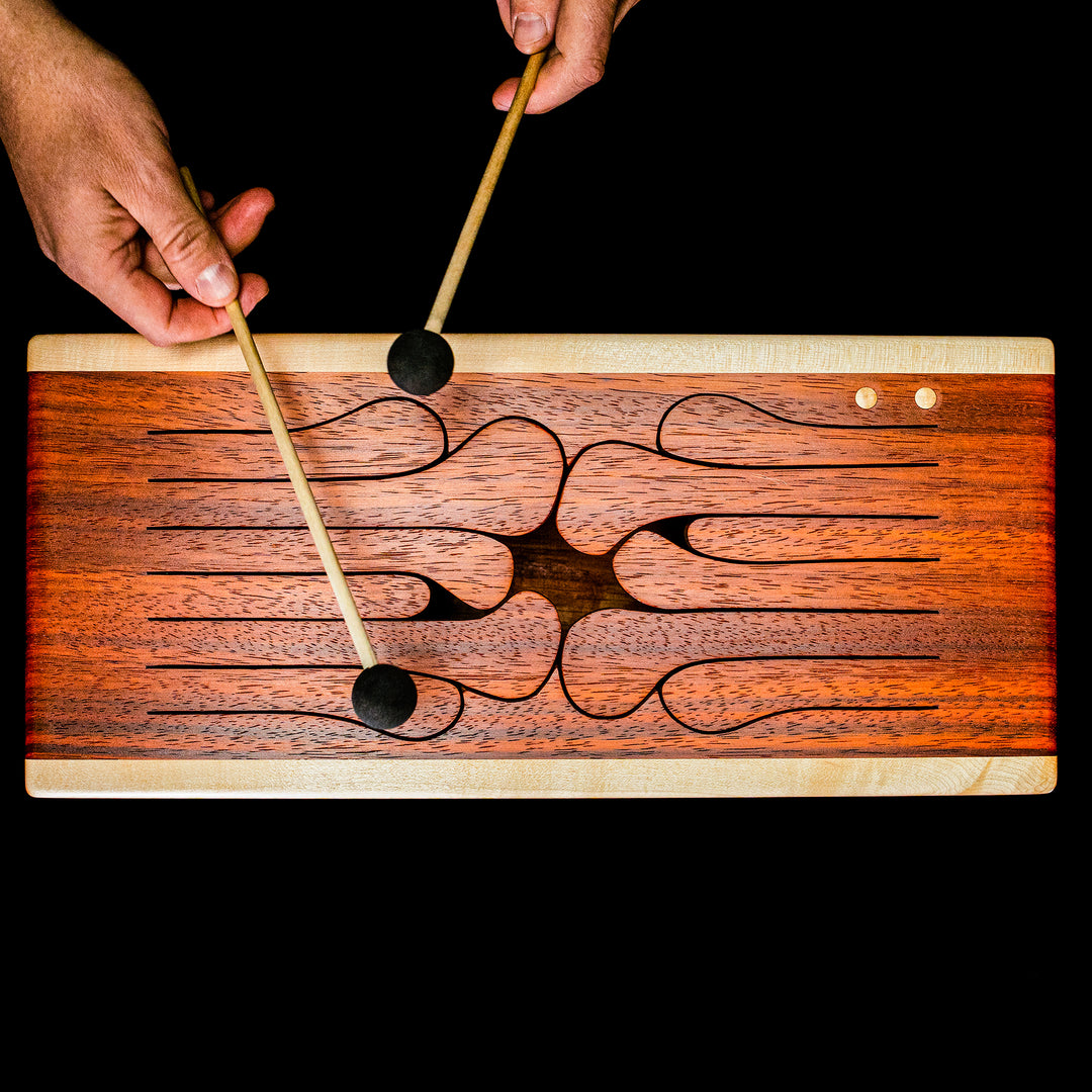 Hands playing 12-key wooden tongue drum with mallets