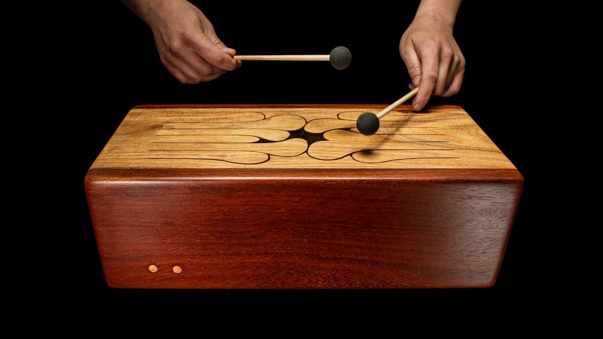 Hands with mallets playing a drum with yellow Canarywood top and red Padauk sides.