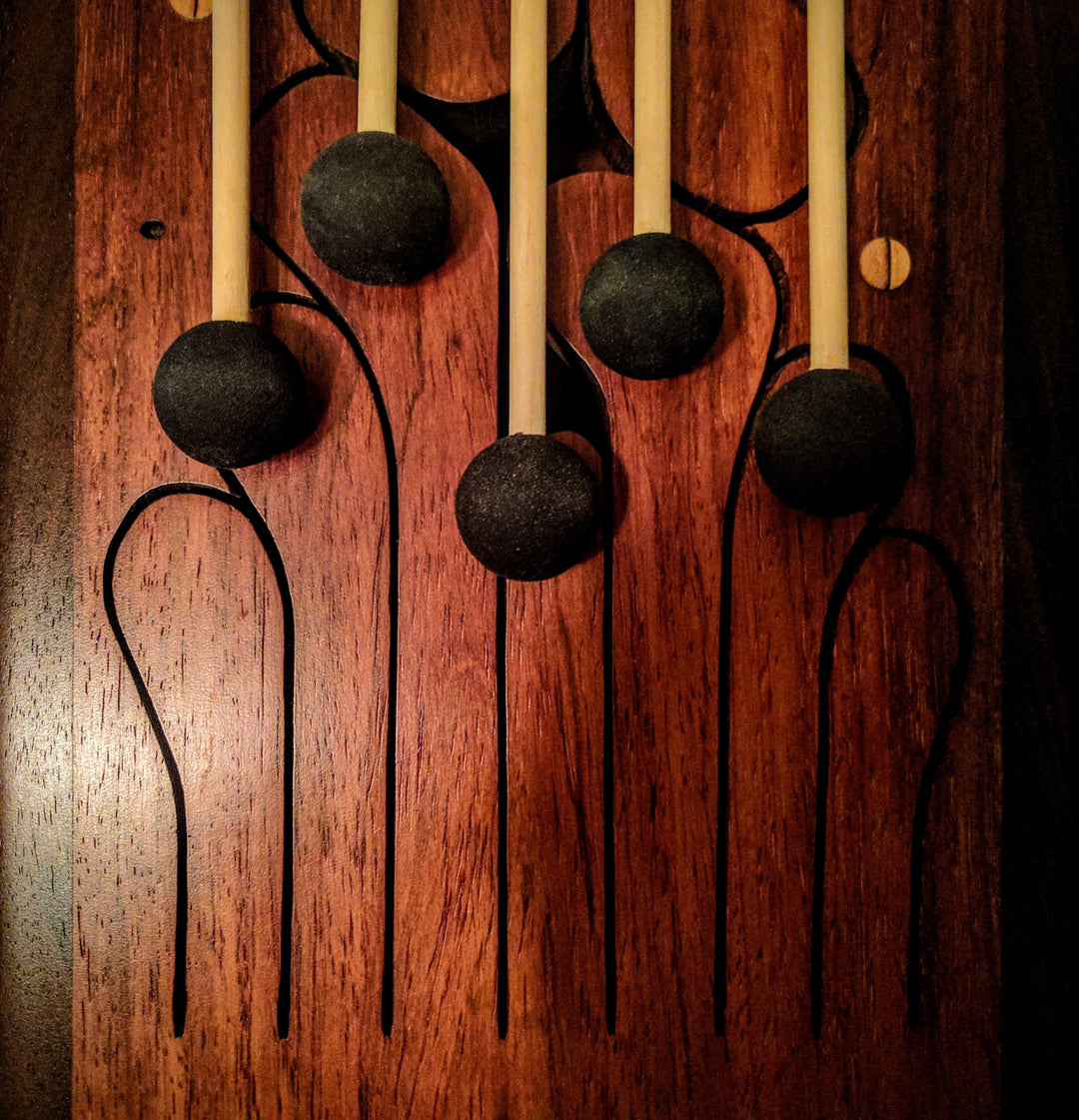 Set of replacement mallets for wooden tongue drum with black rubber heads and natural wood handles placed on a wooden tongue drum surface